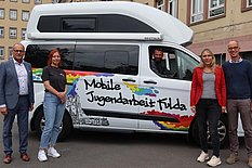 Das Bild zeigt einen Kleinbus und fünf Personen