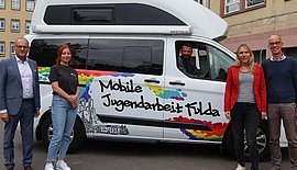 Das Bild zeigt einen Kleinbus und fünf Personen