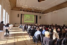 Das Bild zeigt das Publikum im großen Saal der Orangerie beim Festakt zur Eröffnung des Museums.
