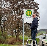Das Foto zeigt einen Mann, der in Oberrode das neue Haltestellenschild anbringt.