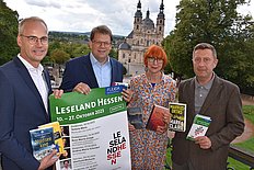 Das Fotoa zeigt vier Personen, die ein Plakat und Bücher in der Hand halten. 